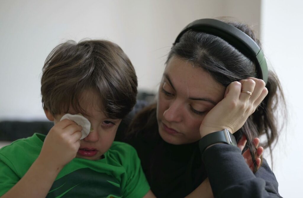 Parent comforts a young child holding a tissue to their eye, showing signs of eye irritation or possible eye injury at home.